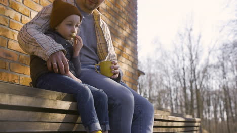 Caucasian-man-talking-with-her-son-while-they-drinking-tea-and-eating-cookies-outside-a-country-house