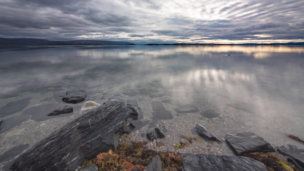 Stormy clouds move fast above the mirrorlike surface of the fjord and the pebble beach as the tide slowly rises