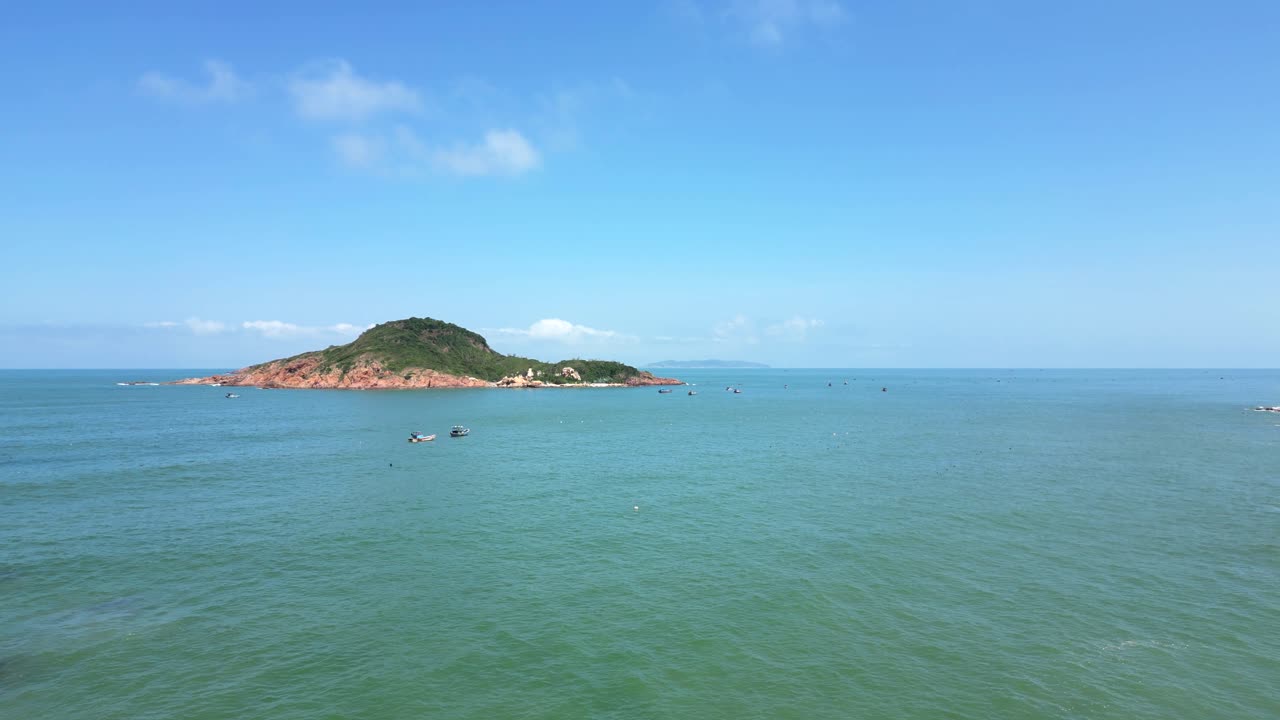 Slow motion rising drone shot over wide open ocean with fishing boats and island