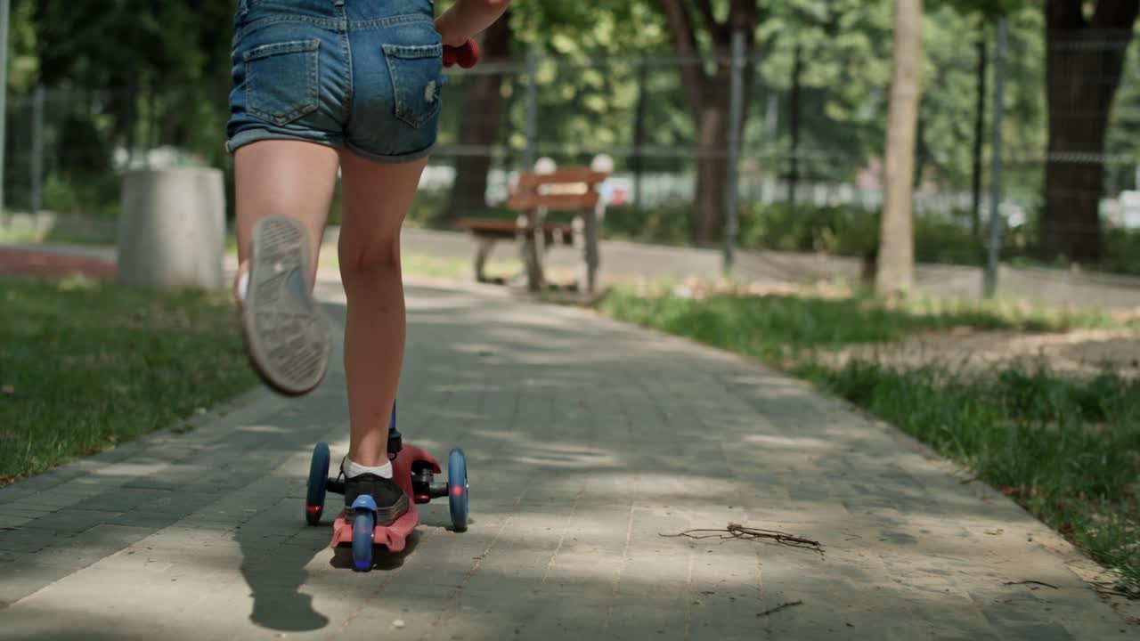 Rear view of girl leaning on push scooter at the park.