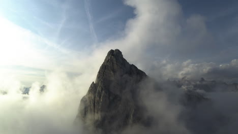 Drone-shot-tilting-toward-a-steep,-rocky-peak-in-middle-of-low-hanging-clouds-in-Dolomites,-Italy