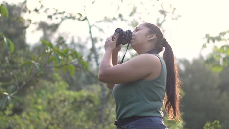 fotógrafa, con una cámara dslr en sus manos, tomando fotografías al aire libre rodeada de naturaleza durante una puesta de sol