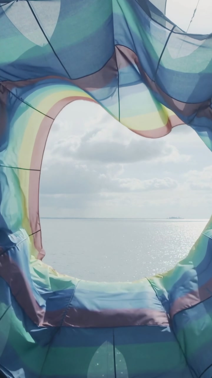 Vertical video: Swaying bright canopy being pushed by wind revealing sunlit sea through star cutout