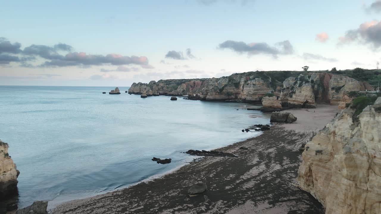 Aerial drone advances above dramatic limestone cliffs and turquoise sea during sunset near Lagos, Algarve