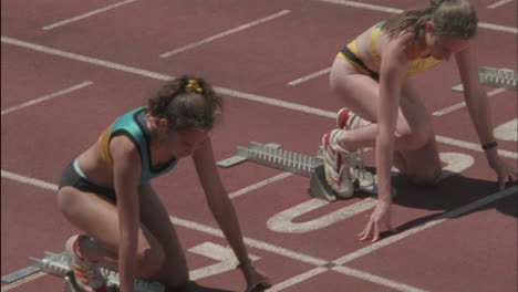 several women runners leave the starting block on a track