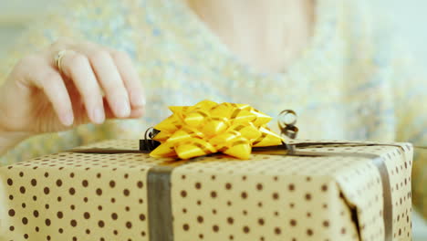 Female-Hands-Adjust-The-Ribbon-And-Bow-On-The-Box-With-A-Gift-Close-Up