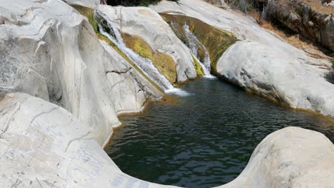 a mountain river with freshwater flowing through a narrow rocky riverbed and forming a small pond