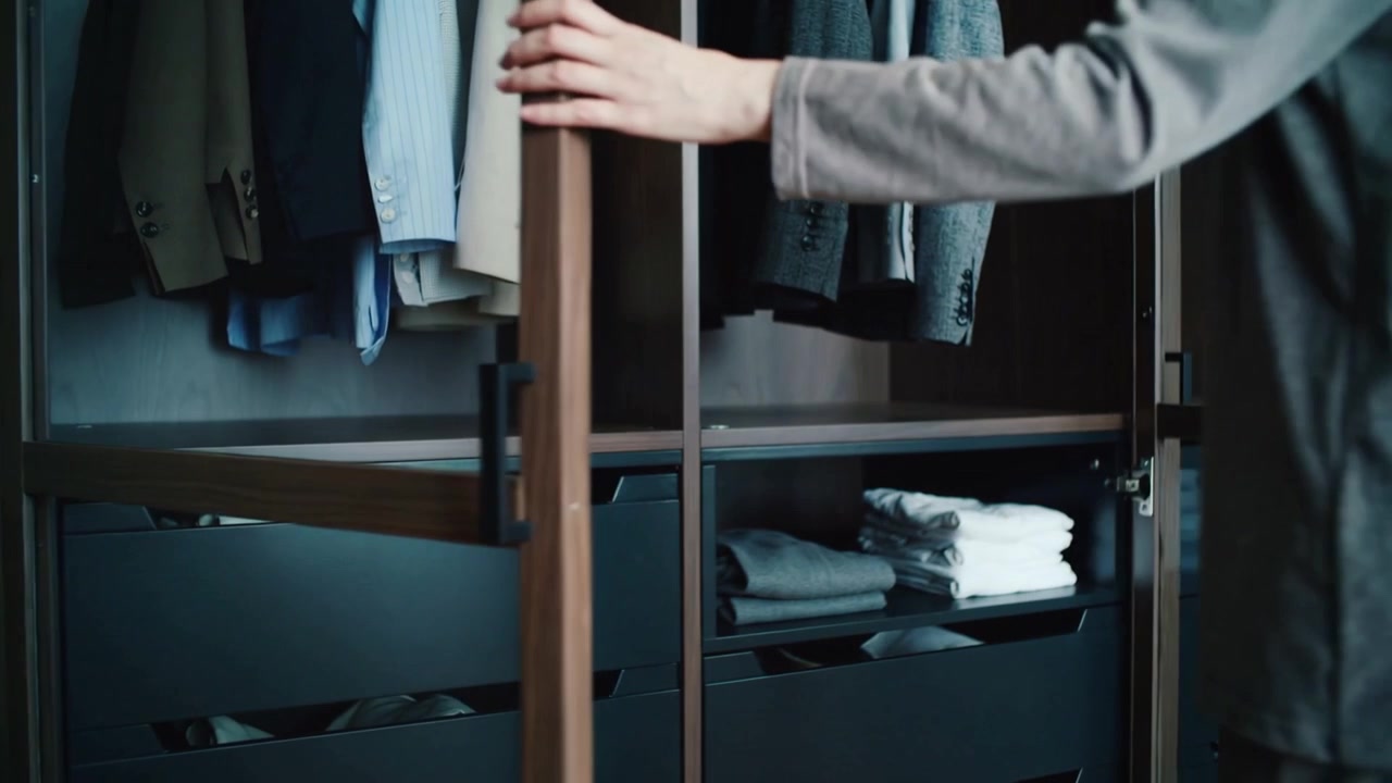 Grasping handles, man in gray outfit opening wardrobe in bedroom to choose outfit, showing jackets