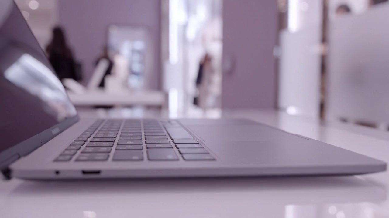 Un laptop dal design raffinato poggia su un tavolo moderno, mettendo in risalto il suo design elegante e le sue funzionalità, posizionato in uno spazio di lavoro contemporaneo ricco di attività.