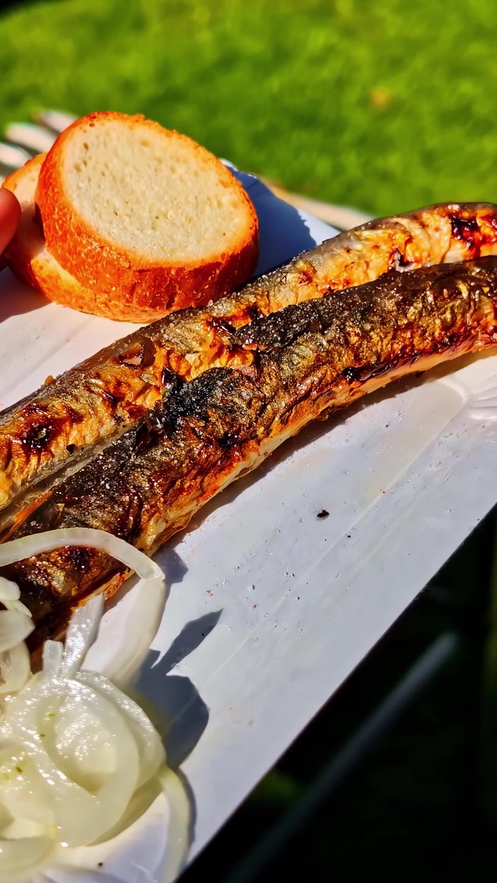 Fresh fish grilling on a barbecue with bread and onions on a plate. Ideal for culinary and outdoor cooking themes.