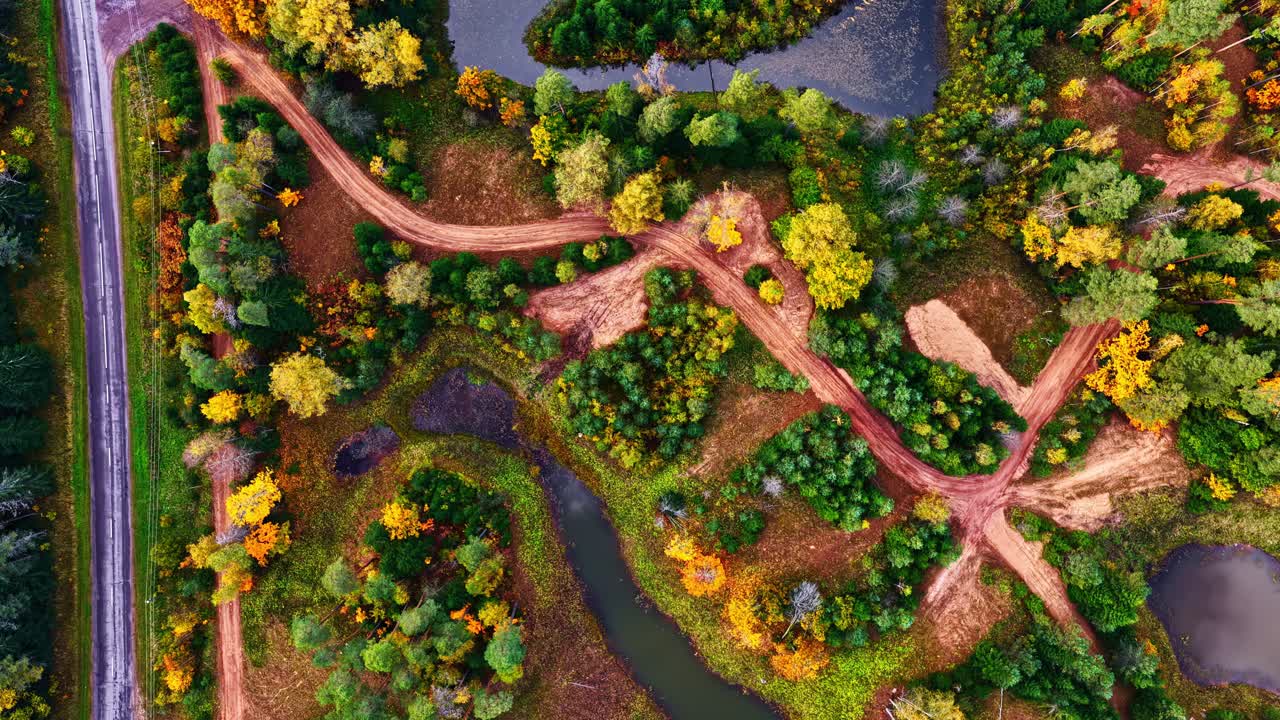 Aerial of small community near forest and lakes with autumn colors in foliage, top down tracking texture above dirt road
