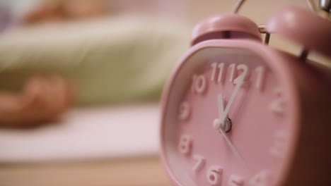 pink alarm clock next to a person in bed