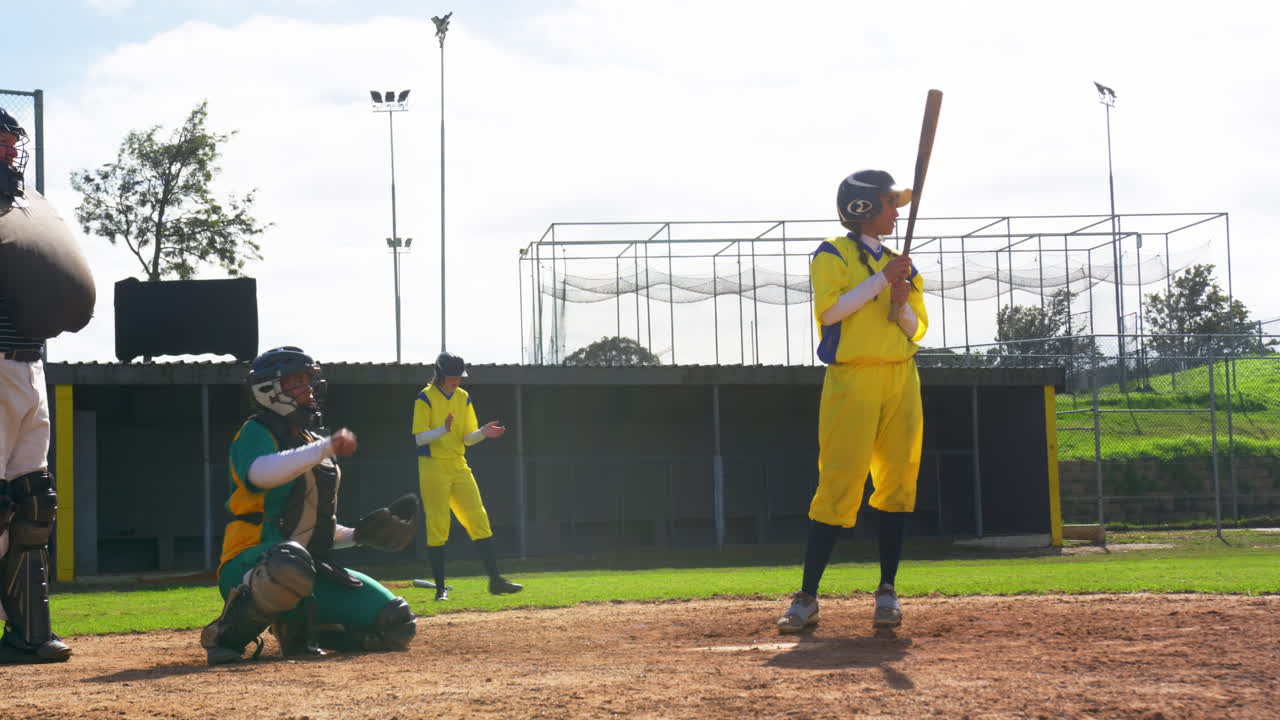 Giocatrici di baseball multirazziali e un arbitro maschio che prendono e lanciano la palla su un campo.