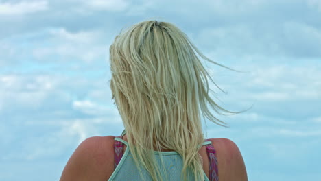 Blonde-girl-in-cyan-tank-top-looking-at-bright-blue-sky-with-clouds