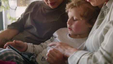 little boy using tablet and chatting with lesbian mothers on bed