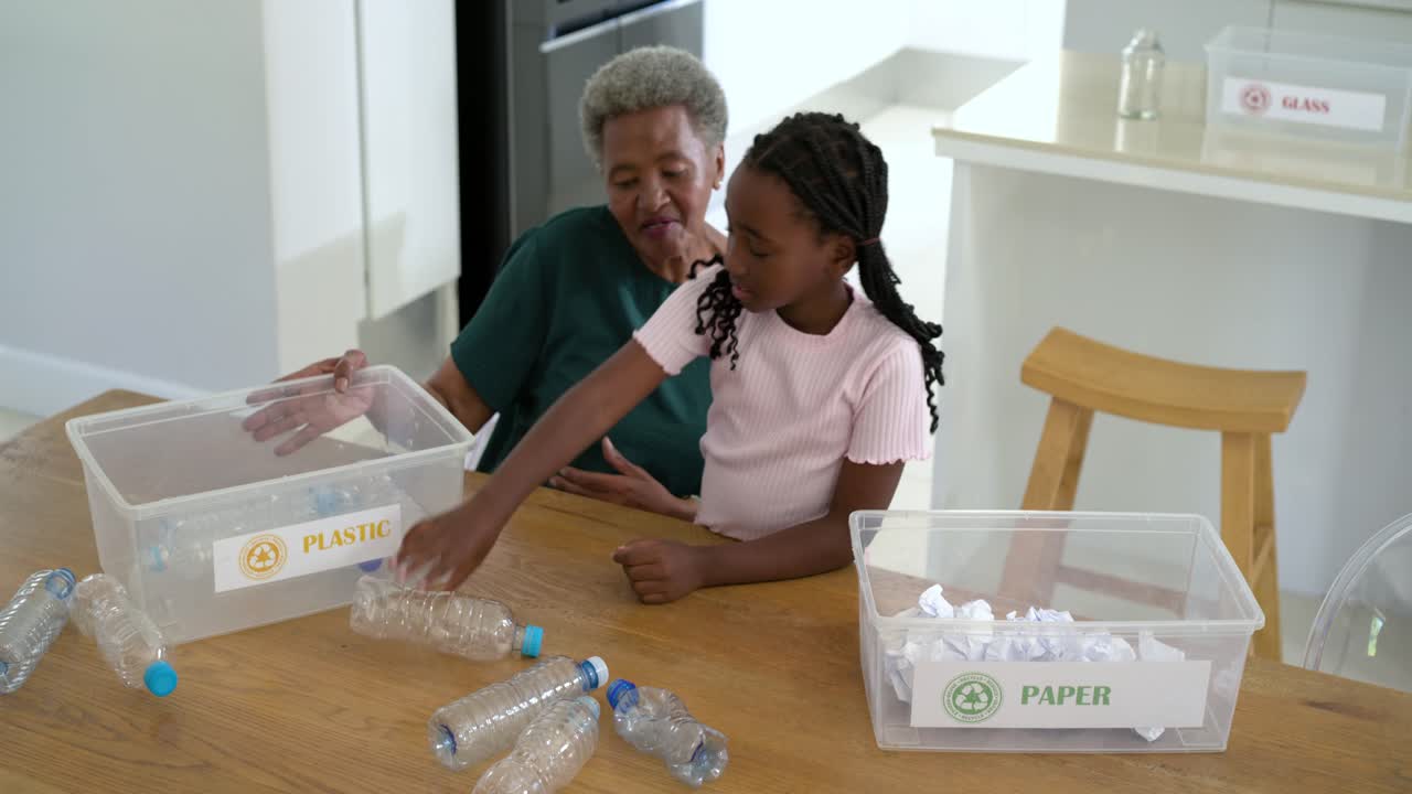 Senior African woman and youth girl guiding, sorting paper, plastic for recycling at kitchen table