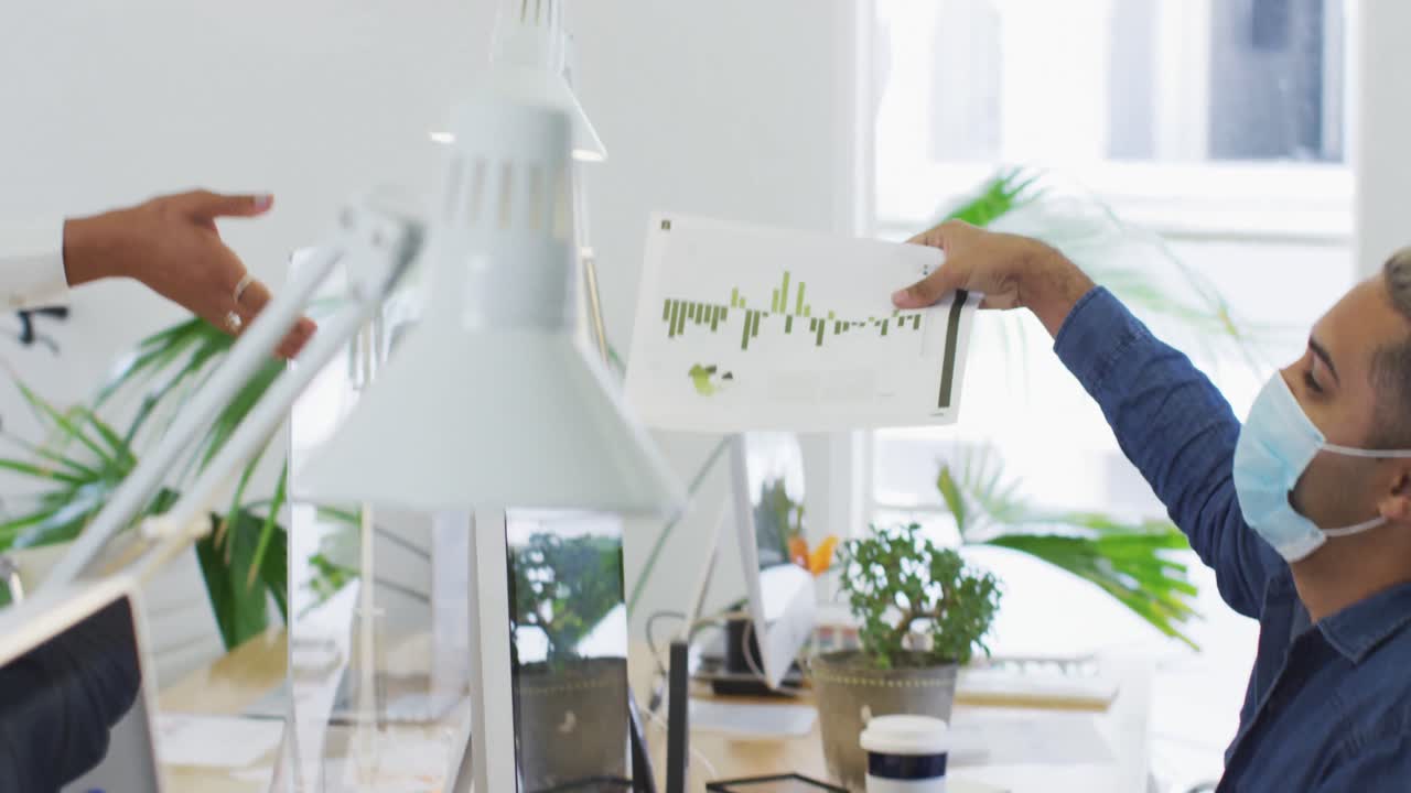 얼굴 마스크를 쓴 남자가 사무실에서 동료에게 문서를 전달하고 있습니다.