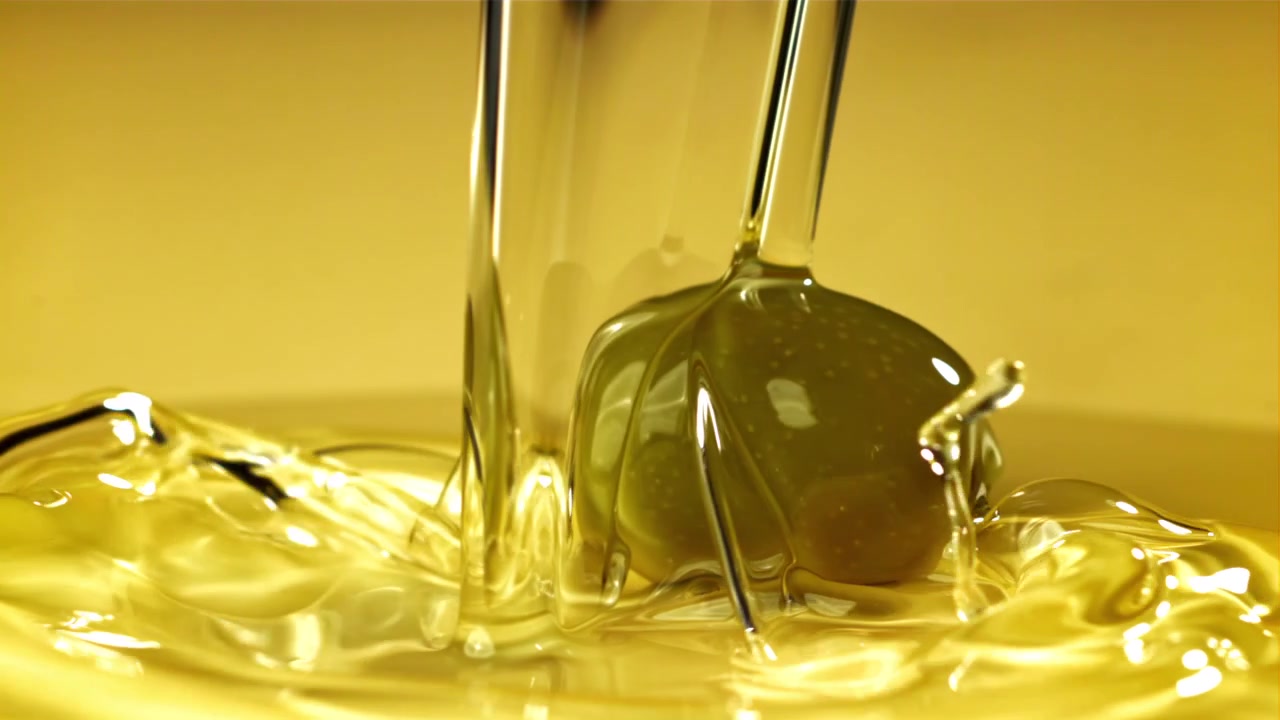 Primo piano di olio d'oliva dorato che cola su un'oliva verde.