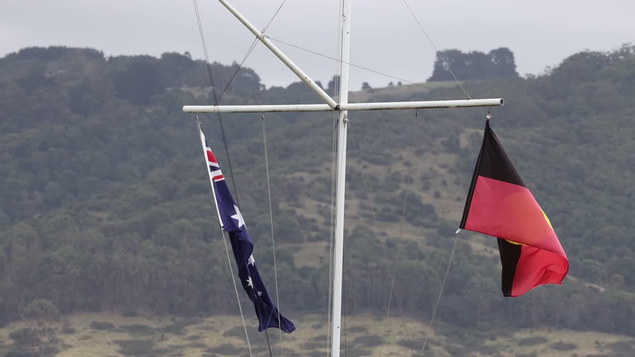 Australian and Aboriginal flags flutter in the wind against a scenic backdrop along the Great Ocean Road