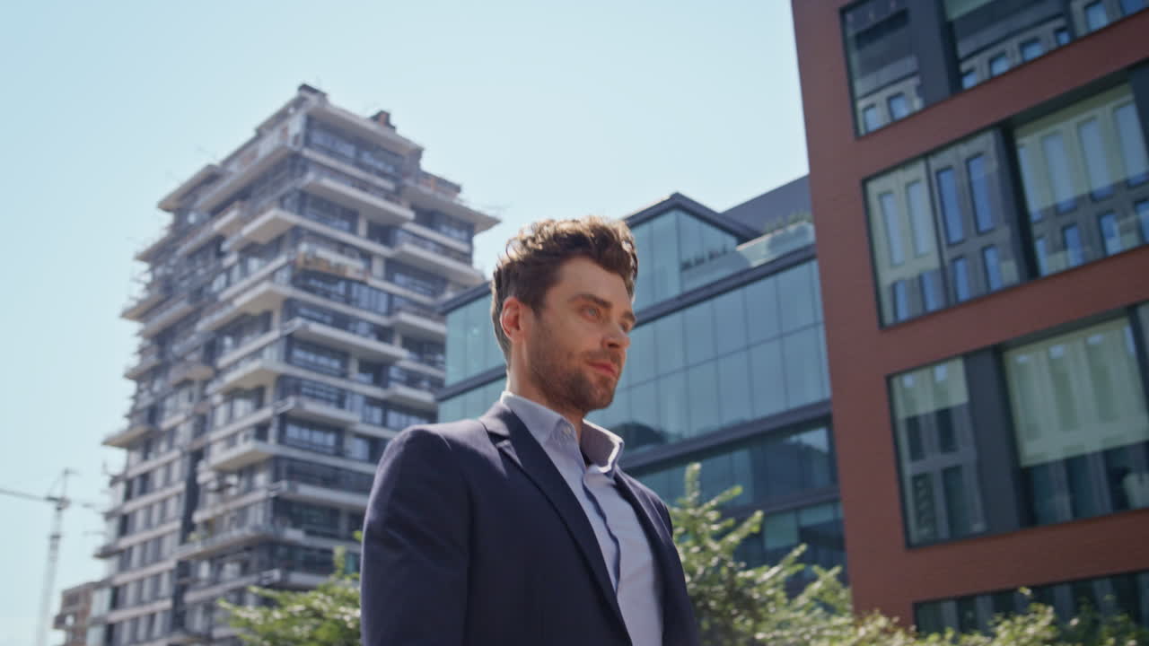 empresario sonriente caminando por una zona de negocios urbana una mañana soleada en traje de cerca.