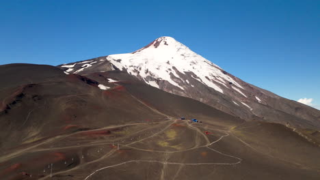 osorno volcano with snow-capped peak, ski resort on volcanic slopes under clear blue sky, los lagos region, chile. aerial forward