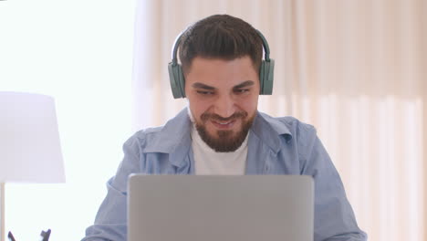 bearded man wearing headphones uses a laptop at home