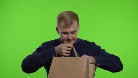 man taking out sale discounts inscription from shopping bags, smiling satisfied with low prices