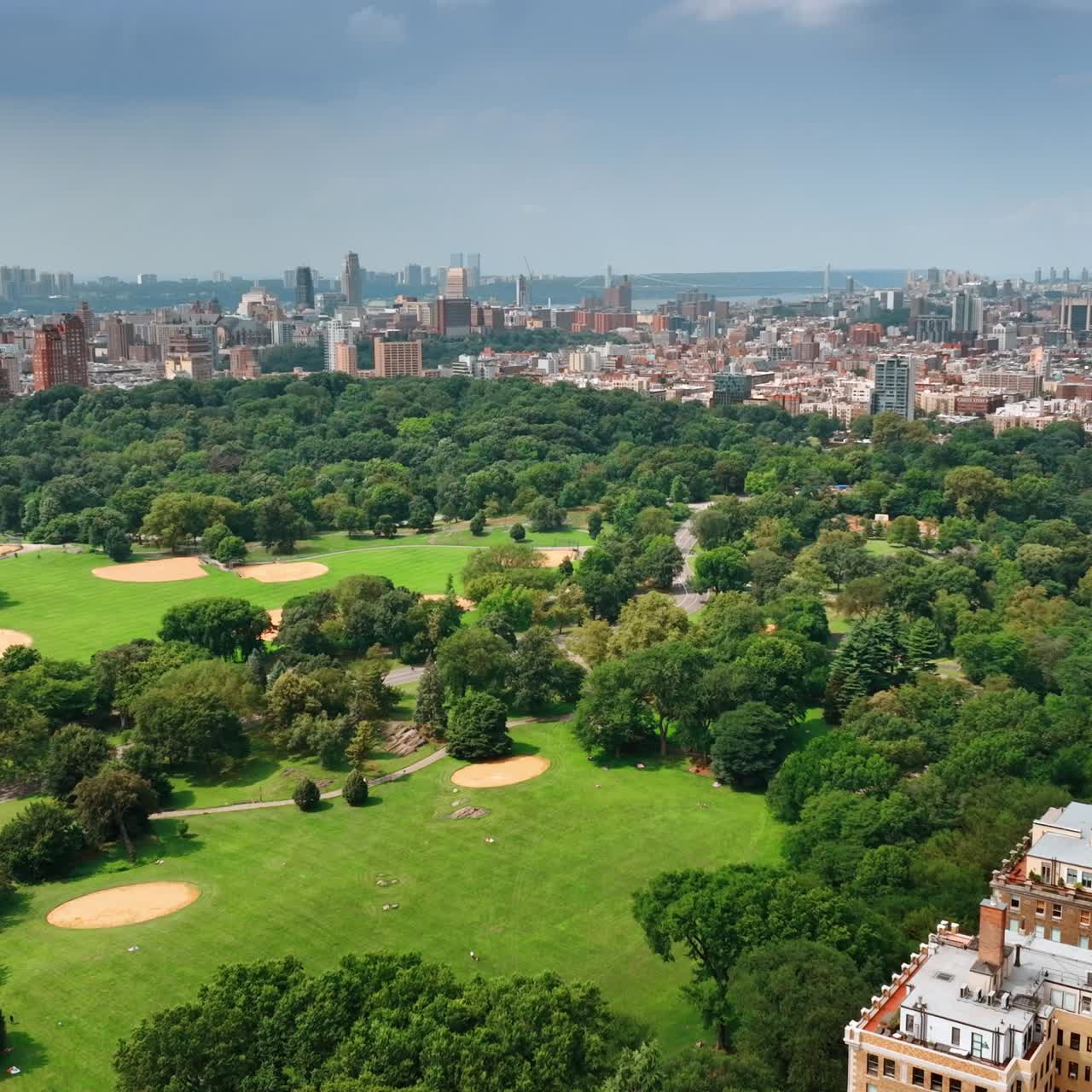 Flying above the territory of the Central Park in New York on sunny afternoon. Densely built cityscape at backdrop. Top view