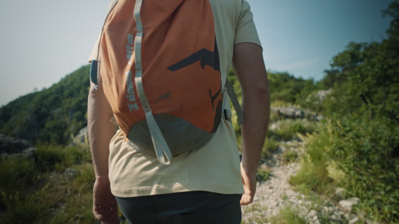 cámara rastreando a un excursionista con una mochila naranja que va desde la perspectiva baja hasta la perspectiva superior