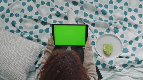 top-view-young-woman-using-tablet-pc-video-chat-waving-hand-enjoying-communication-sitting-relaxed-on-bed-female-watching-green-screen