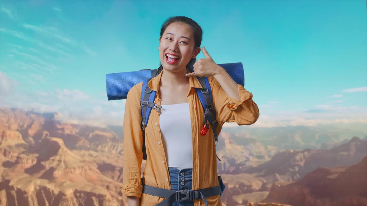 Asian Female Hiker With Mountaineering Backpack Smiling And Showing Call Me Gesture While Traveling At The Top Of Mountain