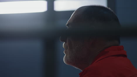 Close-Up-of-Prisoner-in-Orange-Uniform-Holding-Metal-Bars-in-Prison-Cell----------(Stock-Footage)