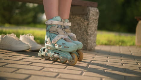 blick auf die beine einer dame in rollschuhen, die auf asphaltiertem boden hin und her rollt, das sonnenlicht wirft schatten mit sneakers leicht hinter sich, mit verschwommenem hintergrundgrün und warmem sonnenlicht