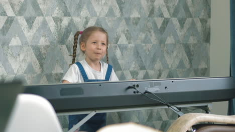 little girl on denim dress plays music synthesizer near wall