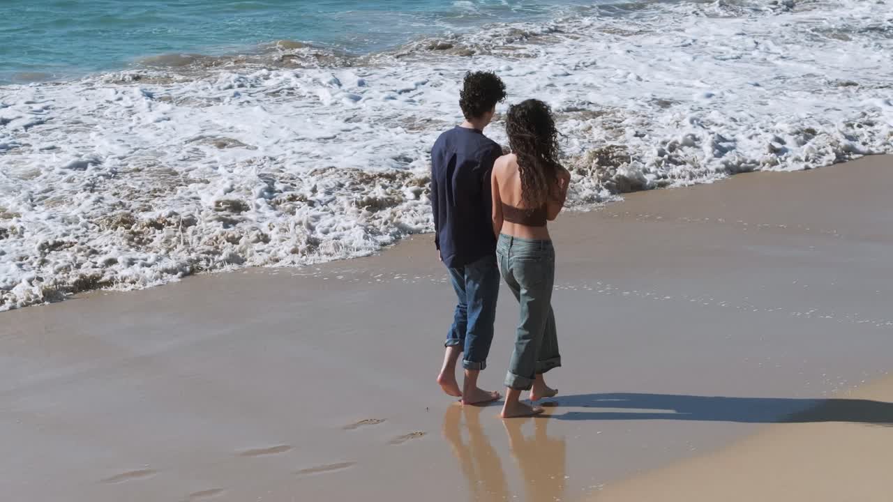 Coppia romantica che si tiene per mano mentre cammina a piedi nudi sulla riva sabbiosa. Ripresa aerea in movimento.