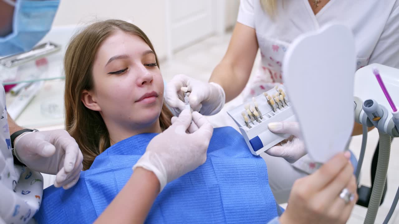 Smiling female patient at dentist's. Stomatologist Choosing the color of tooth to a pretty woman in clinic. Tooth whitening chart.