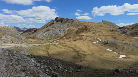 a scenic mountain-top view captured from a moving car, showcasing a rugged landscape of rocky terrain and low grass-covered fields with narrow twisted road. slow motion, sunny day, wide shot