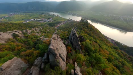 adventurous descending fpv shot capturing mighty stone formations, dürnstein, and its historic ruin surrounded by vineyards and trees