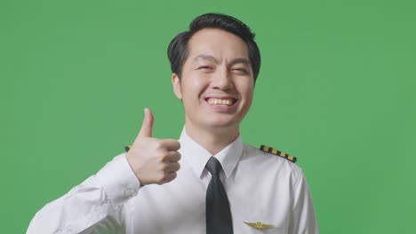 close up of asian man pilot smiling and showing thumbs up gesture to camera while standing in the green screen background studio