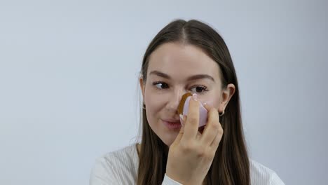 cosmetic makeup foundation being applied with sponge portrait of caucasian woman with beauty or self care routine ready for work