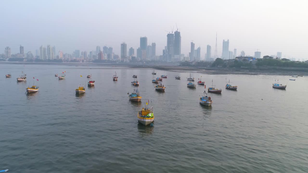Volando sopra le barche dei pescatori parcheggiate al Koliwada vicino al Forte di Worli, rivelando la vista dello skyline di Mumbai con i grattacieli sullo sfondo e gli insediamenti a contrasto.