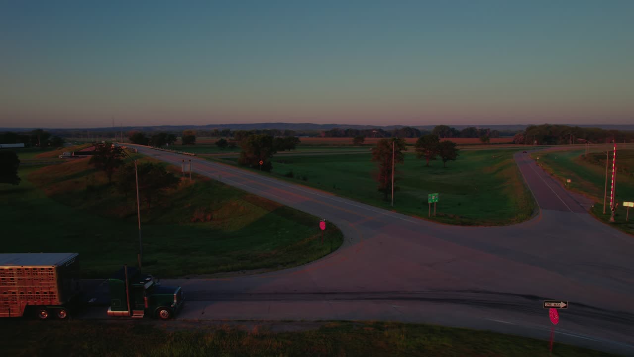 Un rimorchio per bestiame e un classico semirimorchio fermi all'alba lungo la rampa dell'autostrada interstatale. Luce dorata, dolci terreni agricoli, tranquilla mattinata nel Midwest