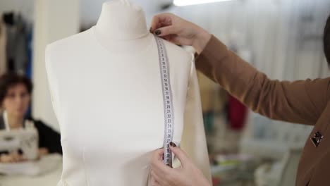 close up of a professional female tailor taking measures with measuring tape on a mannequin while crafting a new fashion cloth. tailor studio. concept: fashion, tailoring, shop. blurred background