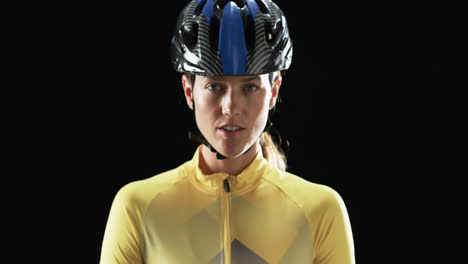 young caucasian woman cyclist in cycling gear poses confidently on a black background