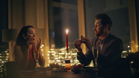 happy guy proposing engagement wedding ring at big windows night hotel closeup