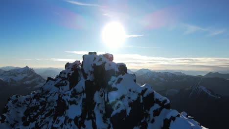 ascending drone shot of bright sun behind snowy peak of mountain in norway - beautiful mountain landscape in winter