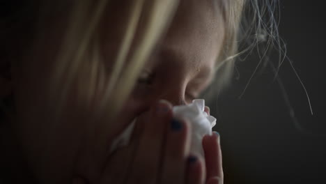 young girl with blonde hair, holding a tissue close to her face, appears to be experiencing emotions, conveying a sense of vulnerability and introspection in a soft-lit environment