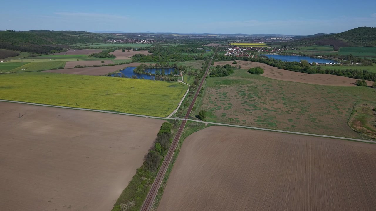 An aerial perspective shows railway tracks crossing through agricultural fields and rural landscape, emphasizing the geometric structure of farmland.