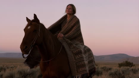 woman riding a horse wrapped in a blanket at sunrise