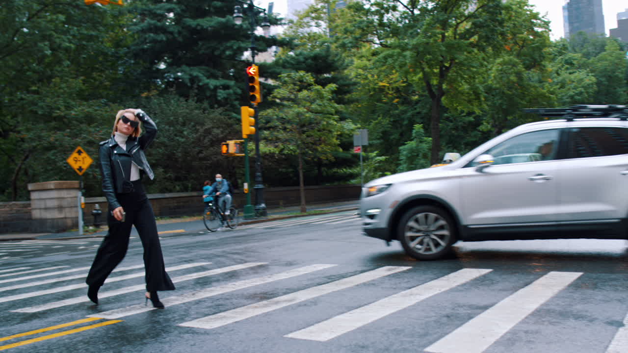 New York, USA, 25 May 2025: Woman crossing the street in New York with yellow taxis. Woman in black trousers and leather jacket walking on pedestrian crossing in Manhattan near Central Park